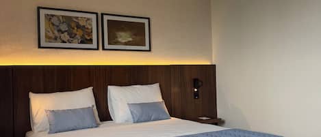 Una habitación de hotel con una cama, una mesita de noche y dos cuadros en la pared.