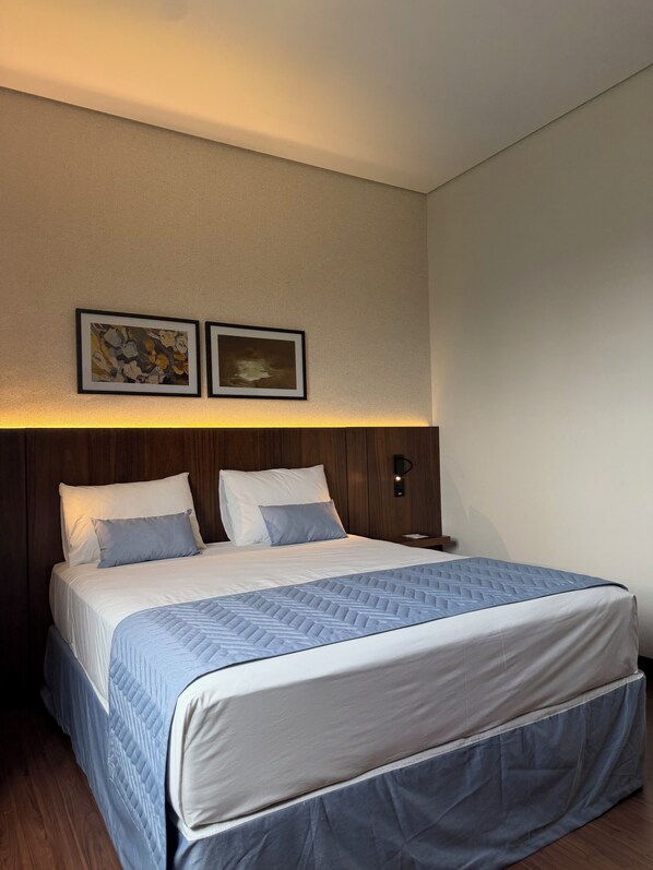 Una habitación de hotel con una cama, una mesita de noche y dos cuadros en la pared.