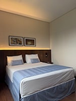 Una habitación de hotel con una cama, una mesita de noche y dos cuadros en la pared.