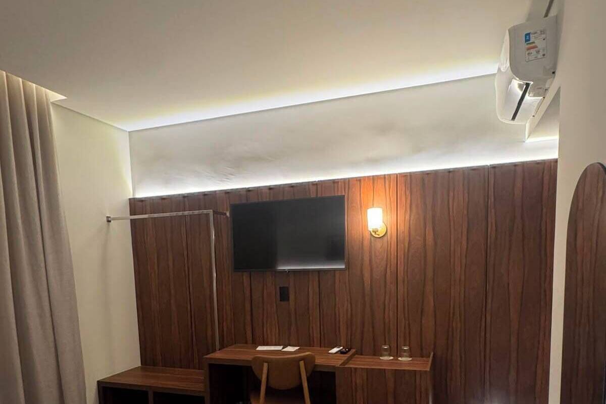 A hotel room with a bed, a desk, a chair, a television, and an air conditioning unit.
