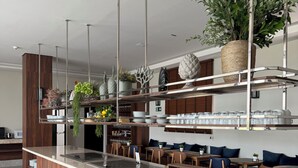 A modern bar area with a wooden counter, shelves with glasses, and seating with blue cushions. - Class Hotel Americana (Americana)