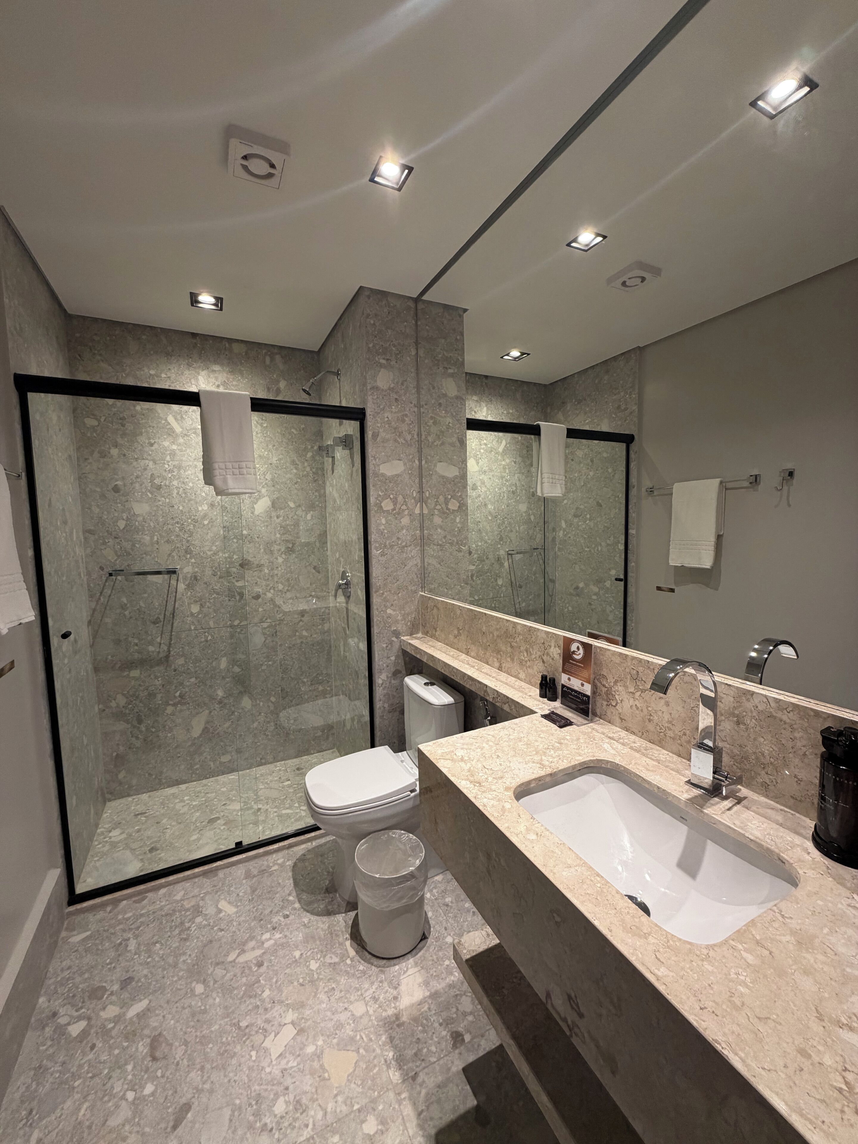 A modern bathroom with a glass-enclosed shower, a white toilet, and a marble countertop with a sink and mirror.