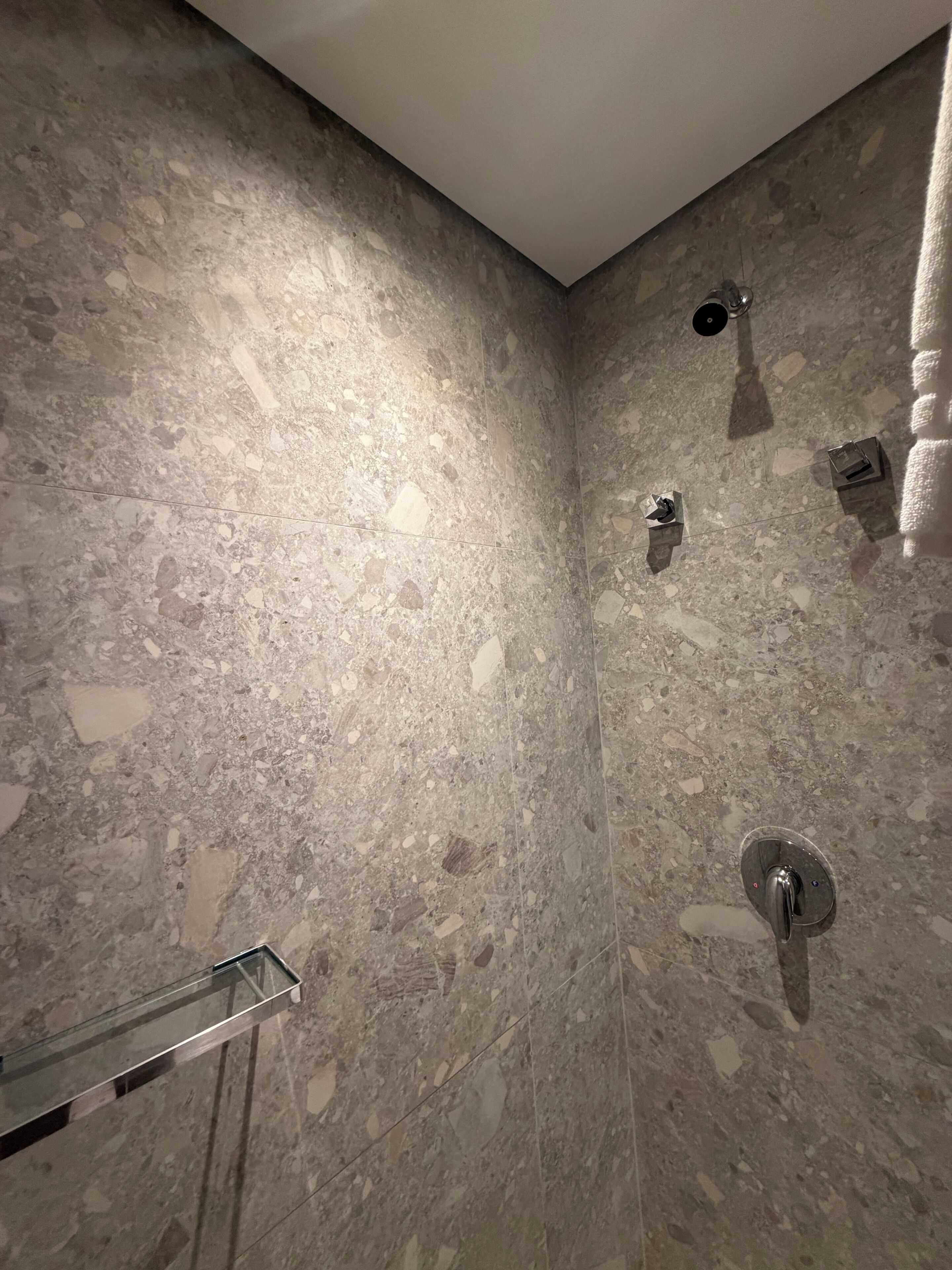 Un baño con pared de baldosas con veteado, cabina de ducha con mampara de vidrio y un perchero.