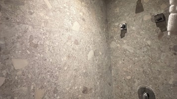 Un baño con pared de baldosas con veteado, cabina de ducha con mampara de vidrio y un perchero.