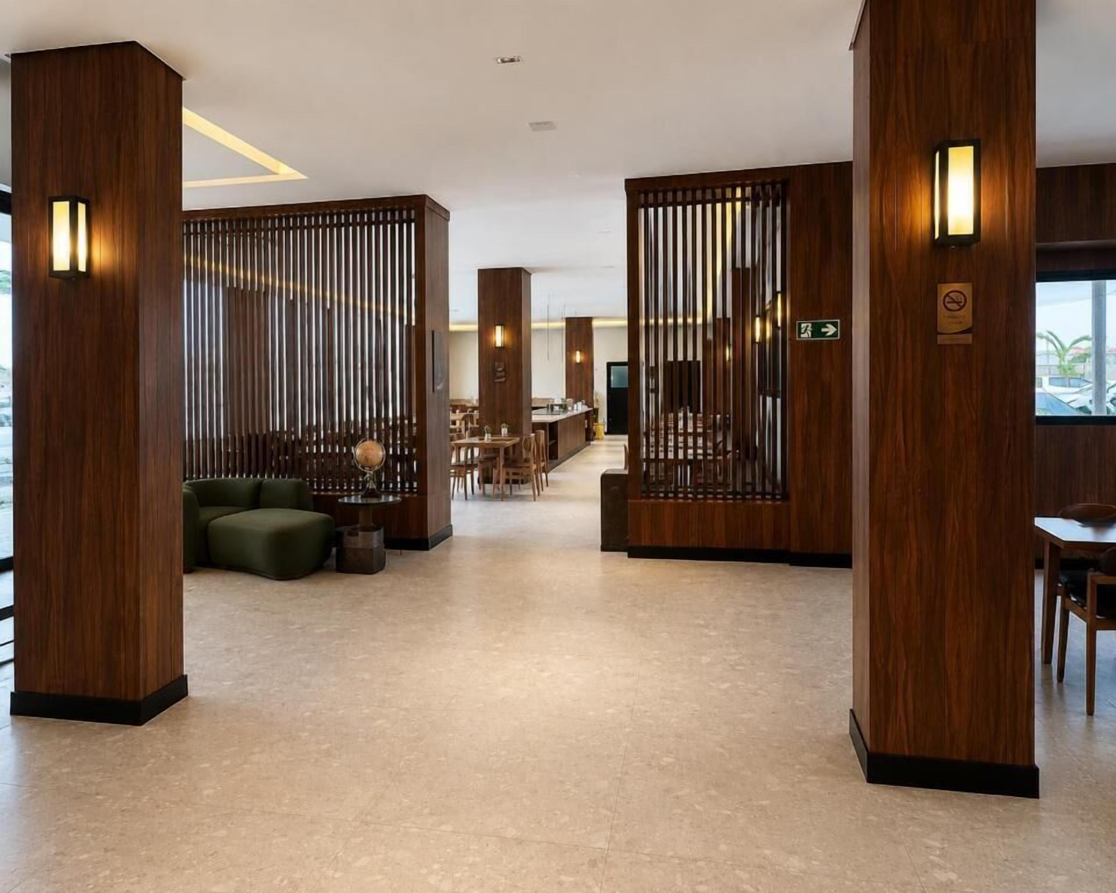 A modern hotel lobby with wooden paneling, a seating area with sofas and chairs, and a reception desk.