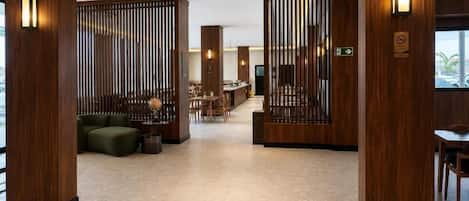 A modern hotel lobby with wooden paneling, a seating area with sofas and chairs, and a reception desk.