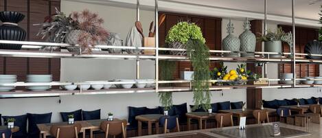 Un restaurante moderno con una isla central, varias zonas de estar y una gran variedad de plantas decorativas.