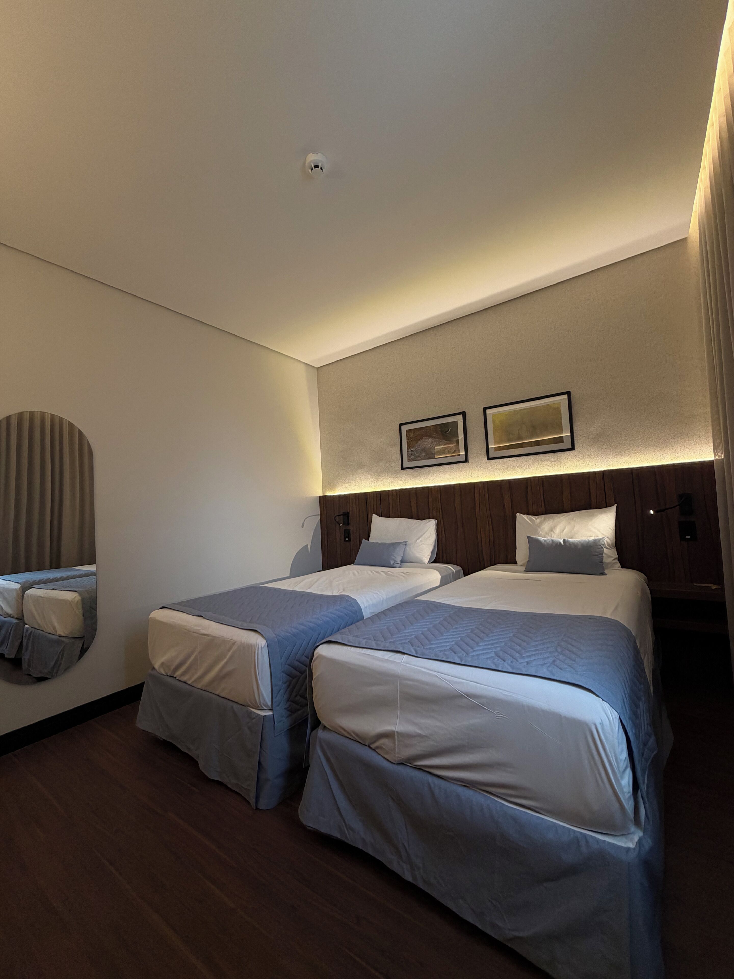 A hotel room with two beds, a large mirror, and two framed pictures on the wall.