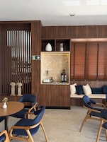 Una habitación de hotel moderna con un separador de madera, una zona de estar con sofá y sillones, una cafetera y una señal direccional.