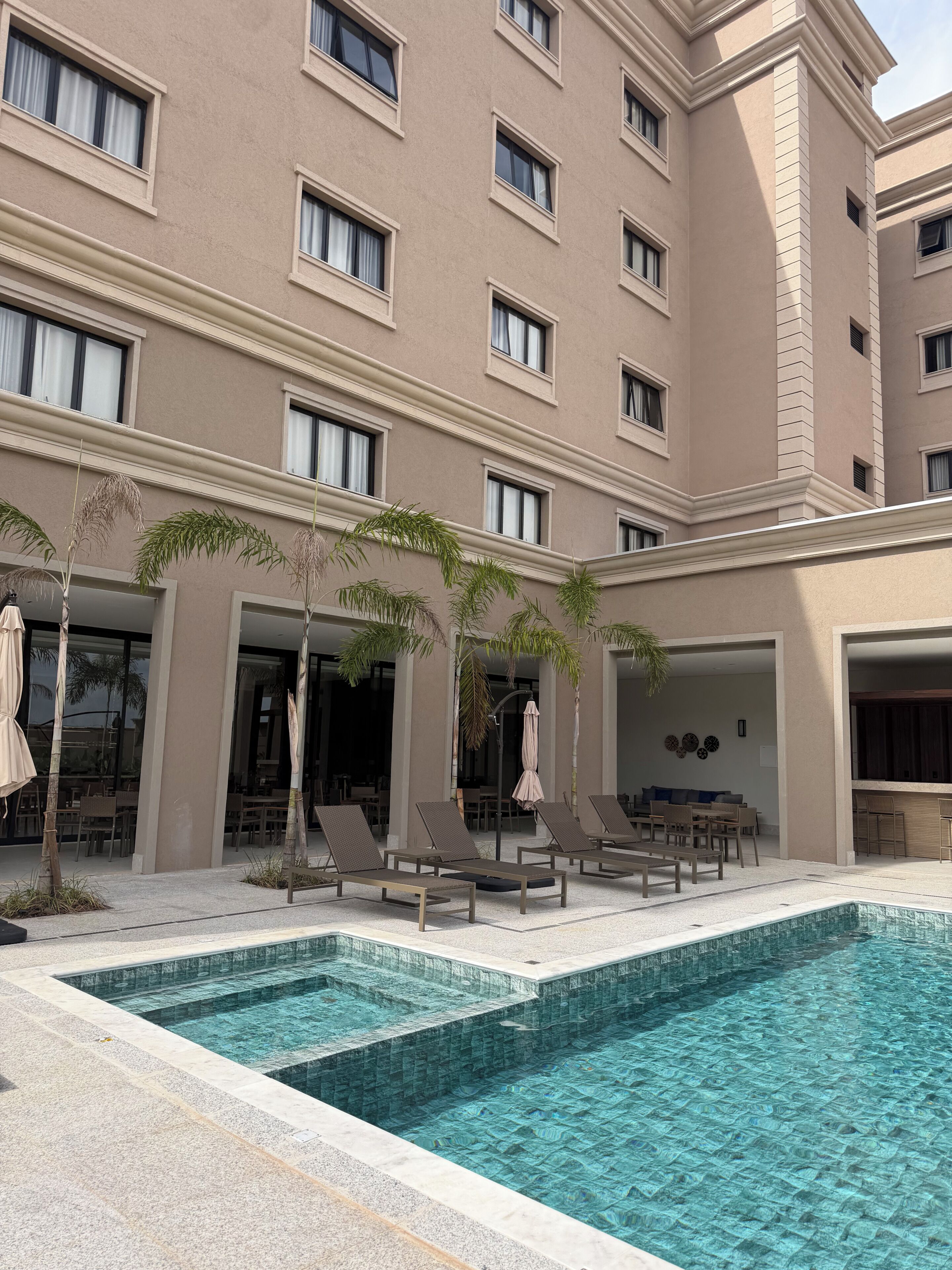 A hotel with a swimming pool, lounge chairs, and palm trees.