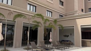 A hotel with a swimming pool, lounge chairs, and palm trees.