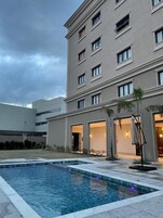 Un hotel con piscina, mobiliario exterior y fachada con varias ventanas.