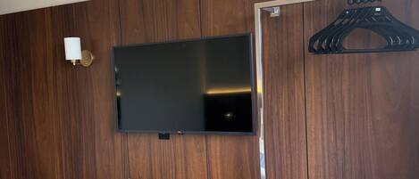 Habitación de hotel con escritorio de madera, silla, televisor de pantalla plana y perchero.