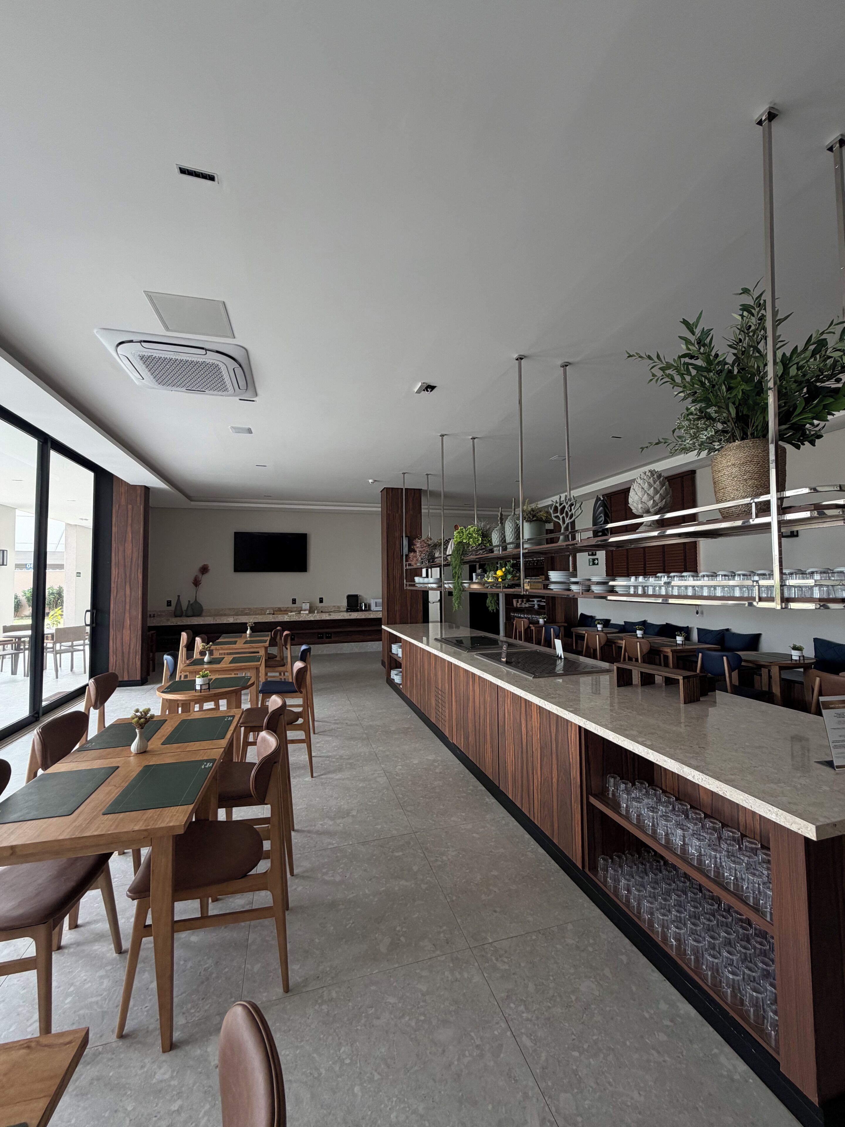 A modern restaurant with a long counter, wooden chairs, and a variety of plants.