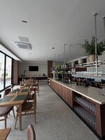 A modern restaurant with a long counter, wooden chairs, and a variety of plants.