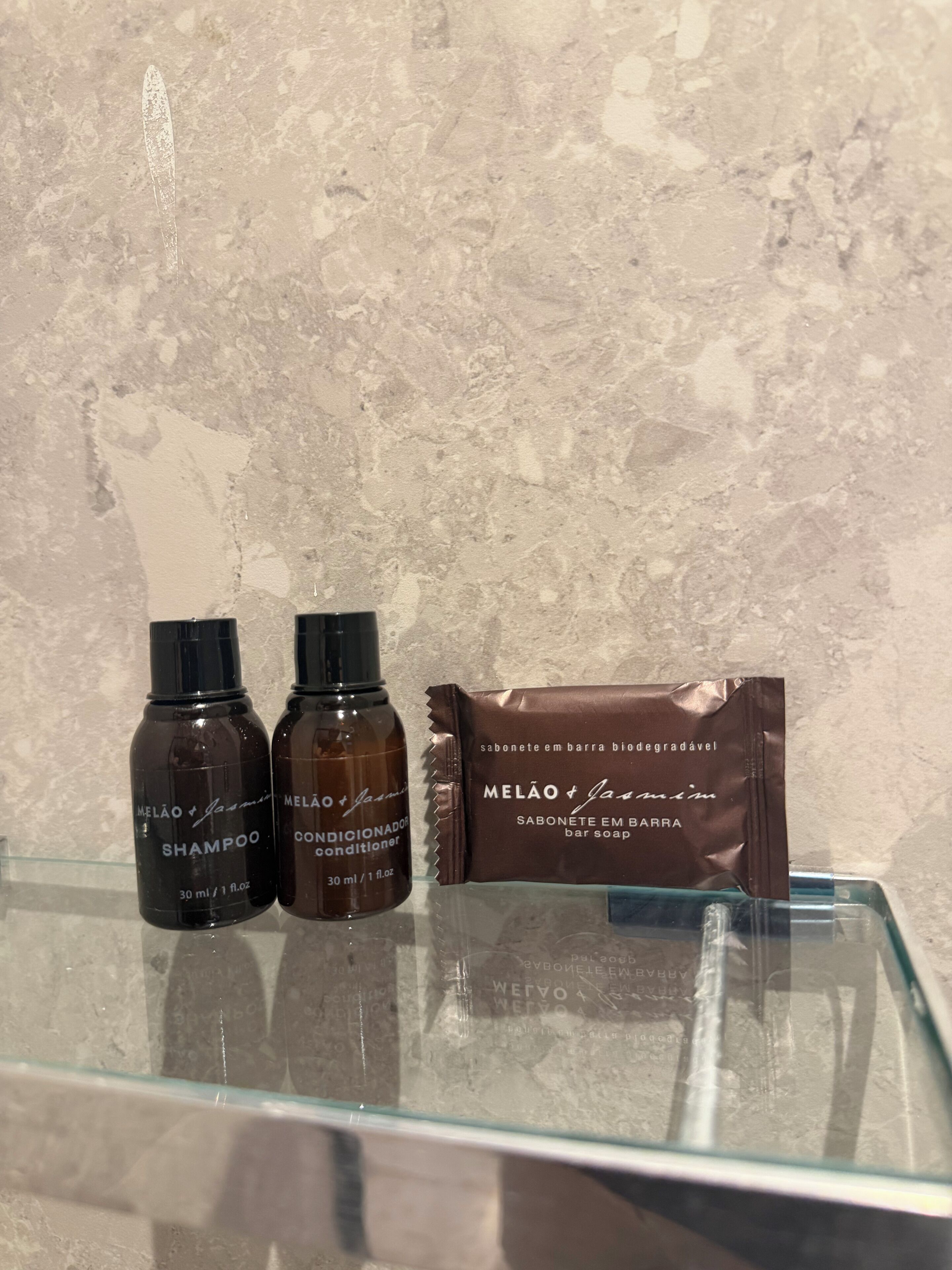 Zwei Shampoo- und zwei Conditionerflaschen sowie eine Seifenpackung auf einer Glasplatte.