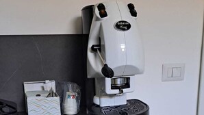 Una cafetera sobre una encimera, una taza de café, un dispensador de pañuelos y un cubo de basura pequeño.