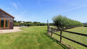 A wooden building with a large glass door, a fenced grassy area, and a picnic table. - Little Owl Barn (Wellington)
