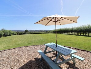 A picnic table with a beige umbrella in a grassy field with a vineyard in the background. - Little Owl Barn (Wellington)