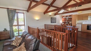 A spacious living area with a leather sofa, wooden railing, and a view to a kitchen with wooden cabinets and a dining table. - Little Owl Barn (Wellington)