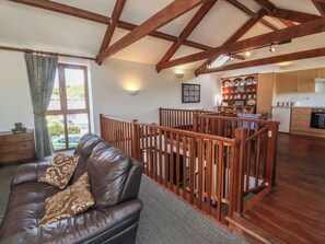 A spacious living area with a leather sofa, wooden railing, and a view to a kitchen with wooden cabinets and a dining table. - Little Owl Barn (Wellington)
