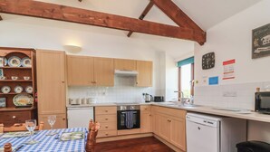 A kitchen with wooden cabinets, a white countertop, a dining table with a checkered tablecloth, and a wooden floor. - Little Owl Barn (Wellington)