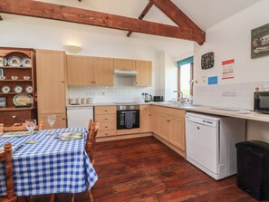 A kitchen with wooden cabinets, a white countertop, a dining table with a checkered tablecloth, and a wooden floor. - Little Owl Barn (Wellington)