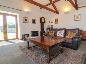A living room with a wooden table, leather sofa, and a fireplace. - Little Owl Barn (Wellington)