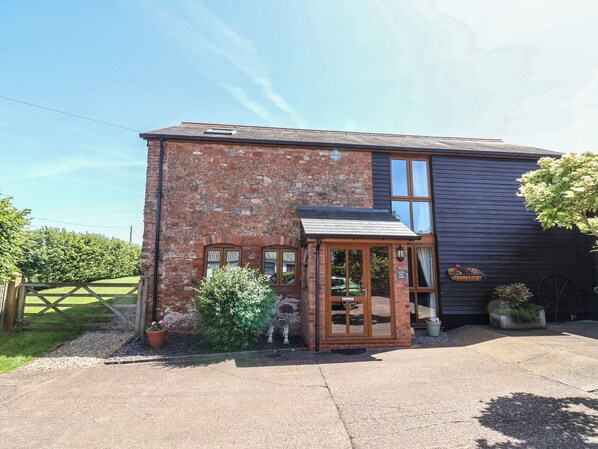 A two-story building with a brick facade, a wooden door, and a small porch. - Little Owl Barn (Wellington)