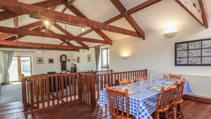 A dining area with a checkered tablecloth, wooden chairs, and a high ceiling with exposed beams. - Little Owl Barn (Wellington)