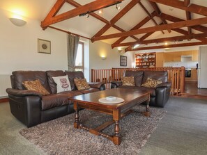 A living room with a wooden ceiling, leather sofas, a wooden coffee table, and a kitchen in the background. - Little Owl Barn (Wellington)