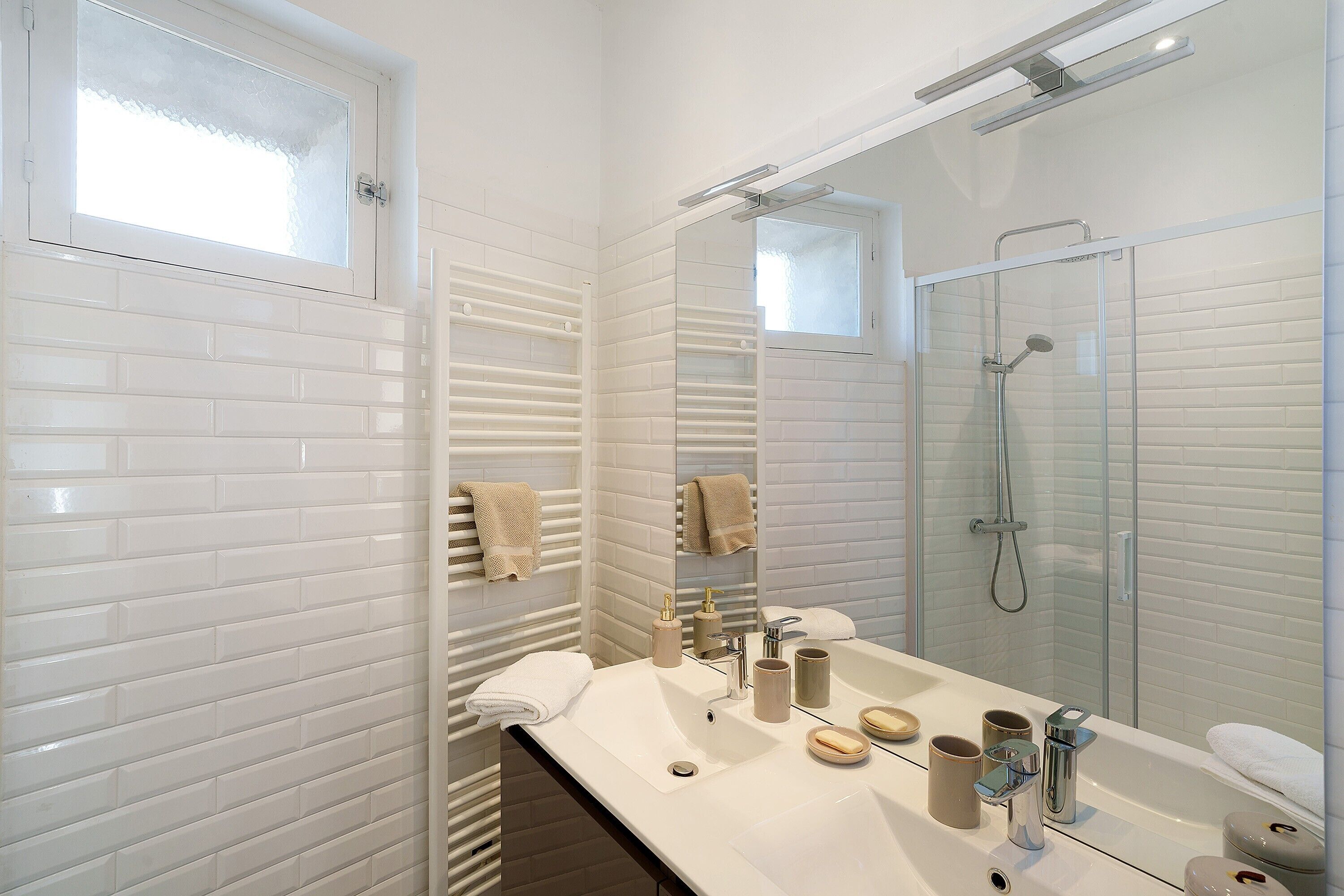 A modern bathroom with white tiled walls, a large mirror, a bathtub, and a shower area.