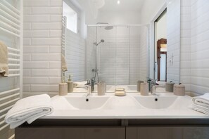Un baño moderno con dos lavamanos, ducha y un espejo grande.