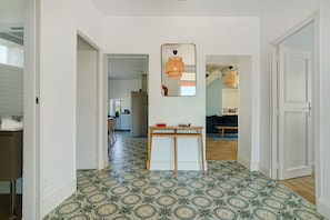 A hallway with patterned flooring, a mirror, a table with a bowl, and a door leading to another room.