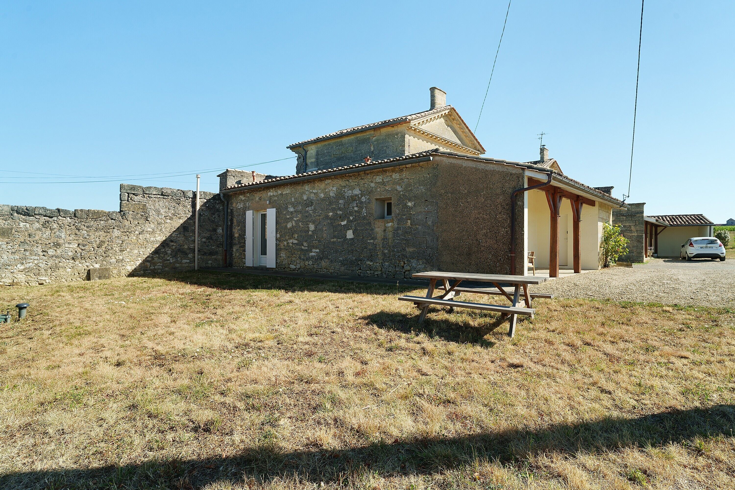 Un bâtiment en pierre avec un toit en tuiles, une porte en bois et une table de pique-nique au premier plan.