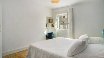 Un dormitorio con cama, una silla, una ventana y una puerta que da a un baño.