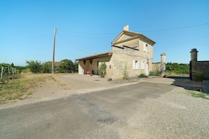 A two-story stone house with a gravel driveway and a metal gate.