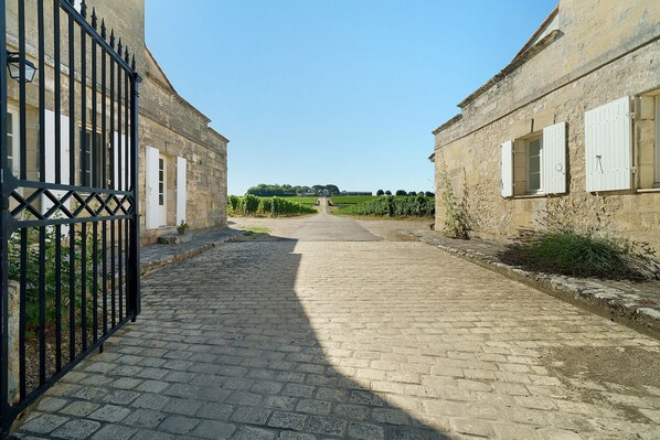 A paved pathway leading to a building with a black metal gate and white shutters.