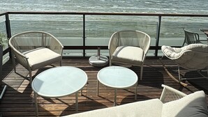 Eine Terrasse mit Korbstühlen, einer Couch und einem Glastisch, mit Blick auf ein Gewässer.