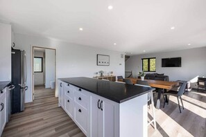 Eine moderne Küche mit Kochinsel, ein Essbereich mit Holztisch und ein Wohnbereich mit Sofa und Fernseher.