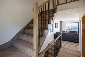 Eine moderne Treppe mit Holzboden und Metallgeländern, die zu einem Wohnbereich mit Meerblick führt.