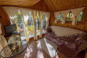 Ein Holzblockhaus-Innenraum mit einer Couch, Vorhängen, einem Fernseher und einem Glastisch mit einem dekorativen Gegenstand.