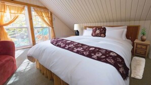 A bedroom with a large bed, a nightstand, a lamp, a chair, and a view of the outdoors. - Domaine Rivière Sacacomie - Le Petit Refuge (Saint-Alexis-des-Monts)