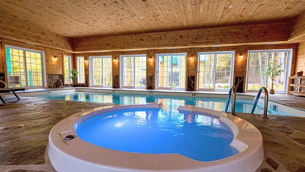 An indoor swimming pool with a hot tub, wooden ceiling, and large windows. - Domaine Rivière Sacacomie - Le Petit Refuge (Saint-Alexis-des-Monts)