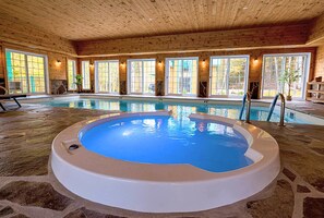 Ein Hallenbad mit Whirlpool, Holzboden und großen Fenstern.