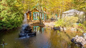 A pond with a waterfall, surrounded by trees and a small wooden structure. - Domaine Rivière Sacacomie - Le Petit Refuge (Saint-Alexis-des-Monts)