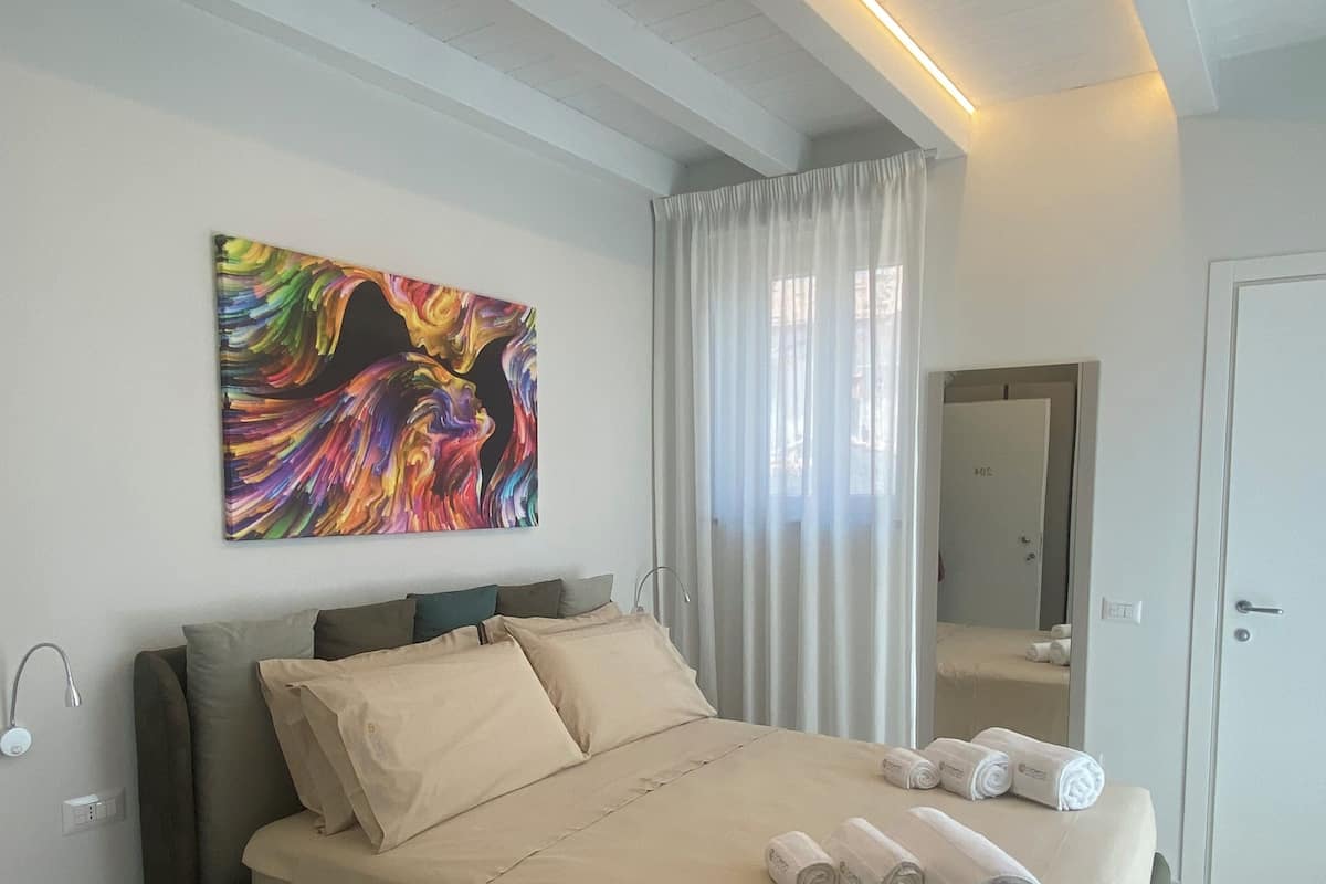 A modern bedroom with a large bed, a painting on the wall, and a bathroom visible through an open door.