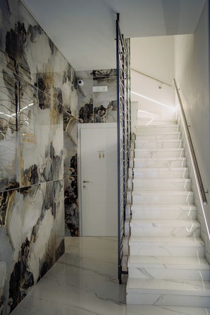 Un interior moderno con una pared de mármol, una puerta blanca y una escalera con barandilla de metal.