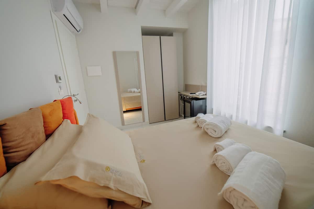 A hotel room with a bed, pillows, a mirror, a desk, and a window with curtains.