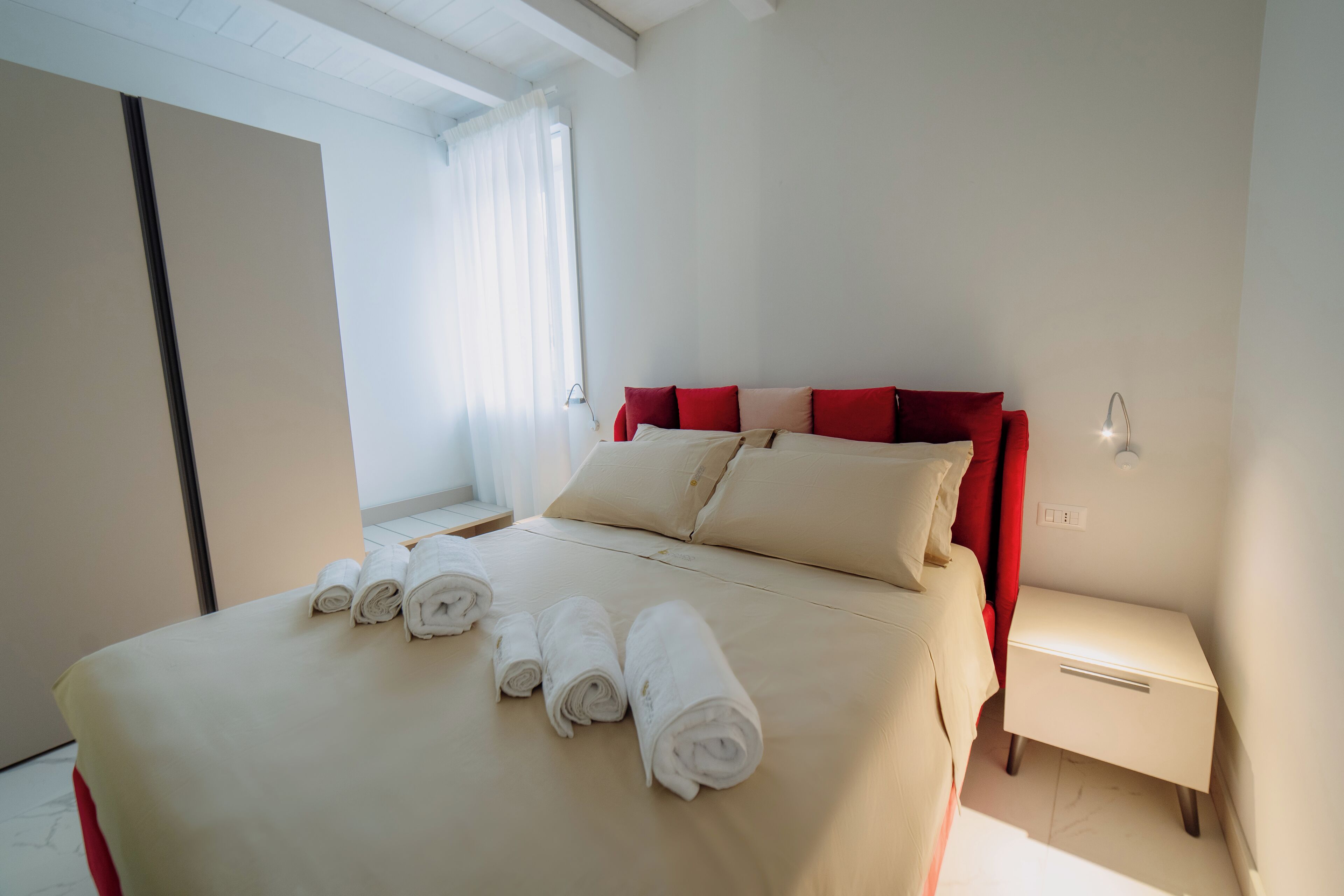 A neatly made bed with rolled towels, a bedside table, and a nightstand in a hotel room.